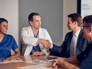 A medical doctor and a business man shaking hands in a group setting